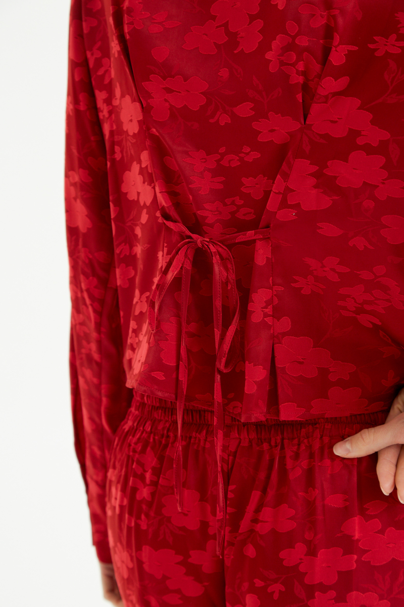 Camisa roja satinada de jacquard floreado con pinzas de entalle en frente y espalda, con lazo para regular. 