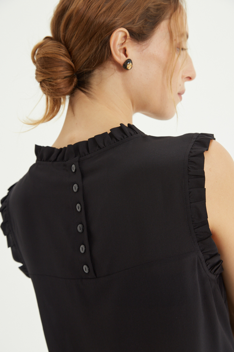 Musculosa negra de seda con volados en cuello y sisas, de corte recto y larga a la cadera con cuello mao y botones en la espalda. 
