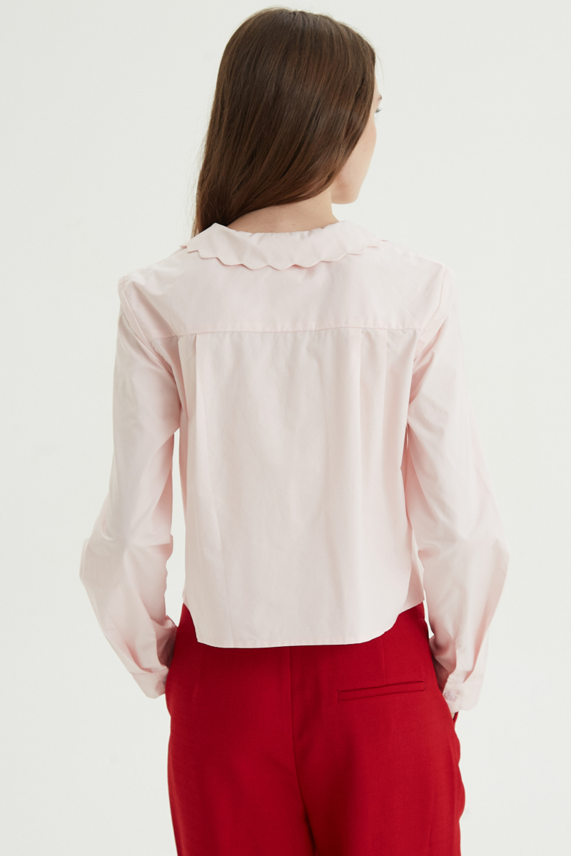 Camisa rosa de poplin de largo hasta la cadera con terminación en forma de onditas en cuello, puños y cartera y botones a tono en forma de flor. 