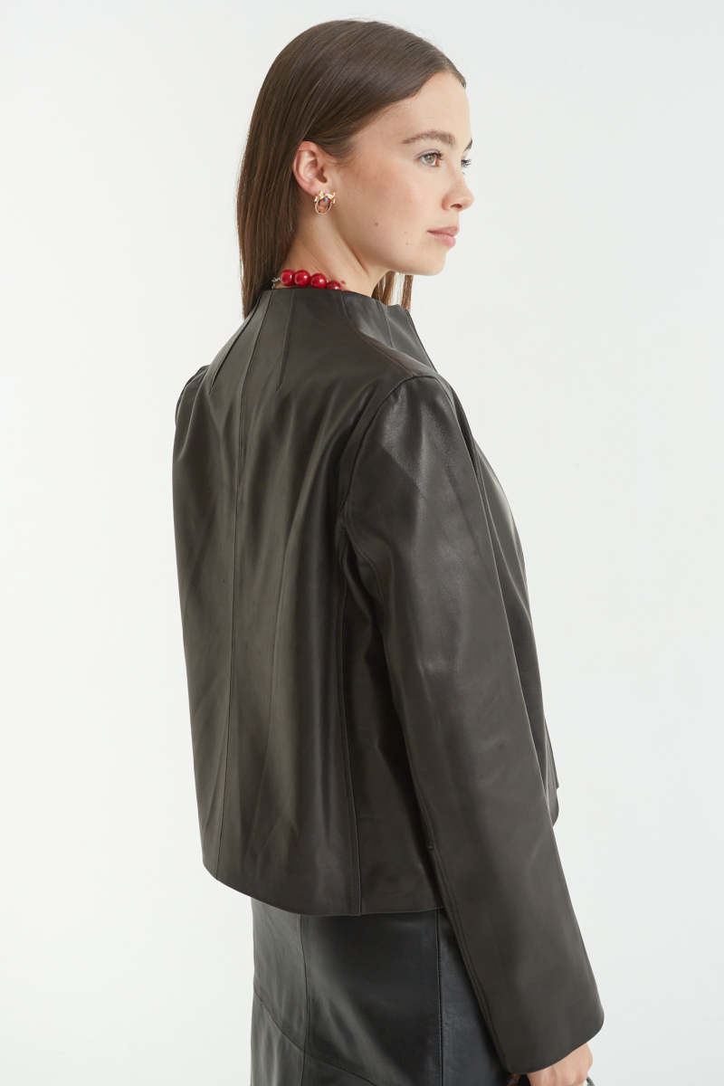 Campera de cuero negro con cuello alto y cierre metálico, de calce recto y larga hasta la cadera.
