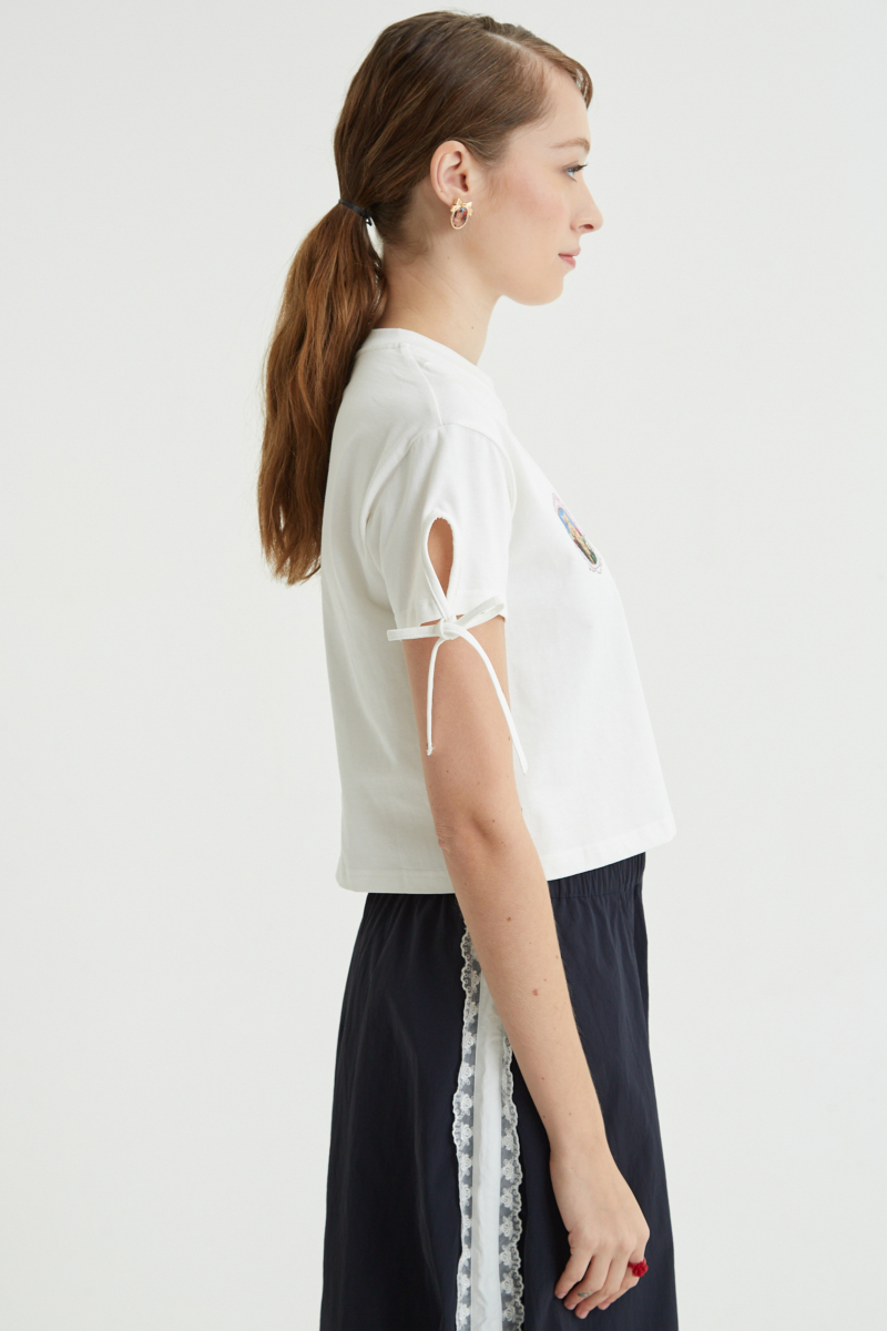 Remera blanca suelta y crop de algodón estampada con lazos en las mangas para atar en moño.
