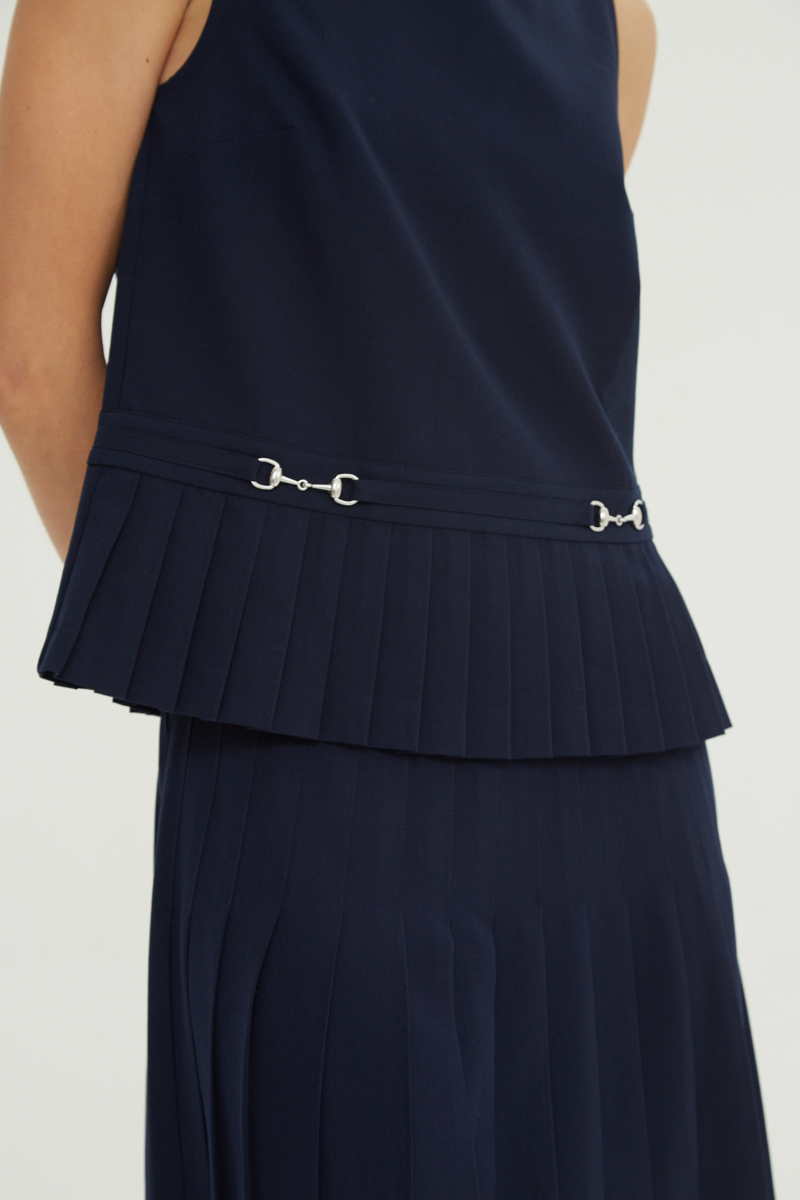 Blusa azul sastrera sin mangas con tablas en la cintura, herrajes metálicos y escote a la base del cuello, larga a la cadera. 