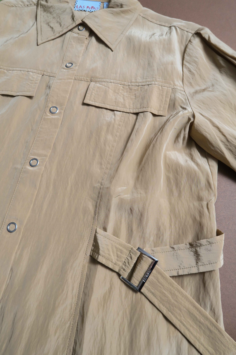 Camisa beige manga larga con textura arrugada y brillo sutil, bolsillos con solapa y cinturones en la cintura. 