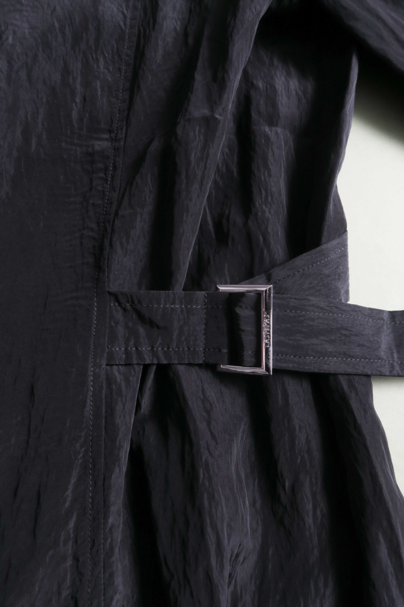 Camisa negra manga larga con textura arrugada y brillo sutil, bolsillos con solapa y cinturones en la cintura. 