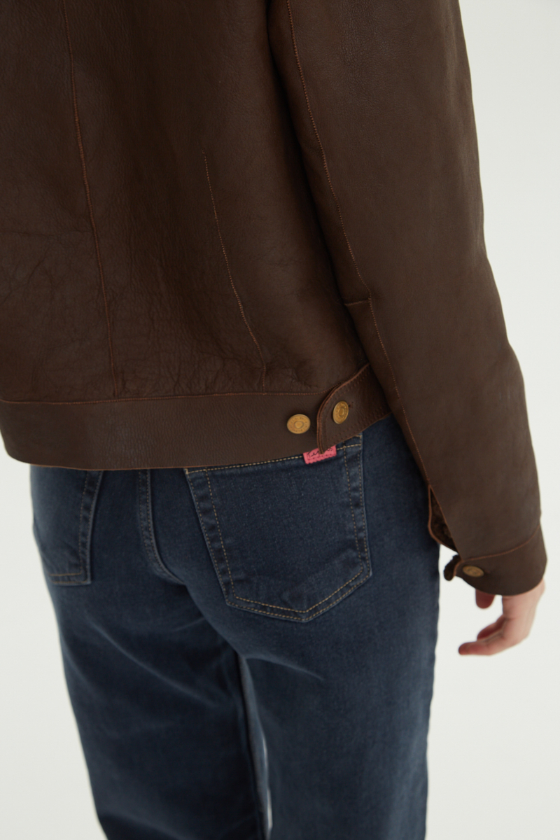 Campera de cuero marron con interior de pelo afelpado, recta y larga a la cadera con botones chatos metalicos y solapas frontales que simulan ser bolsillos. 