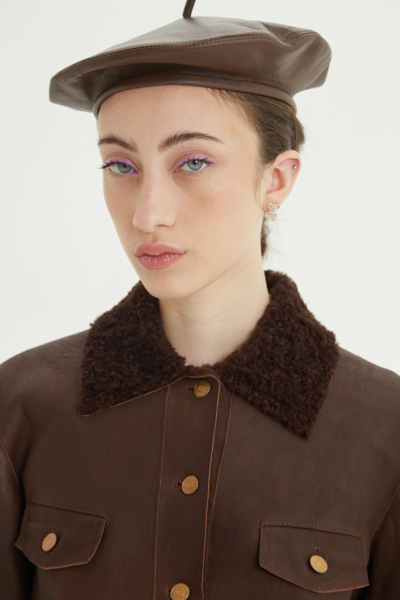 Campera de cuero marron con interior de pelo afelpado, recta y larga a la cadera con botones chatos metalicos y solapas frontales que simulan ser bolsillos. 