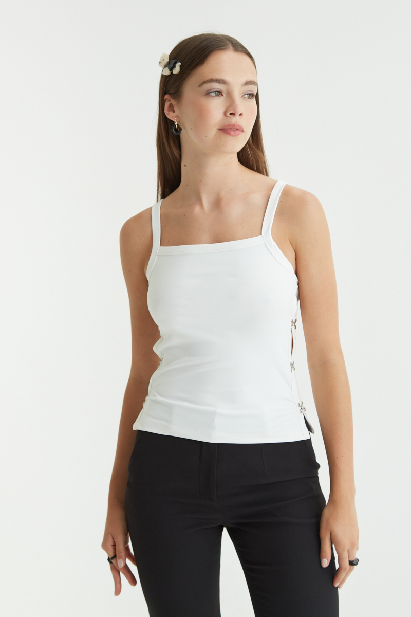 Musculosa blanco al cuerpo de punto elastizada con aberturas laterales unidas por ganchos peleteros y escote cuadrado