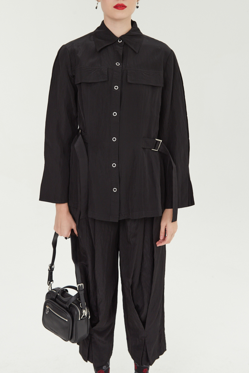 Camisa negra manga larga con textura arrugada y brillo sutil, bolsillos con solapa y cinturones en la cintura. 