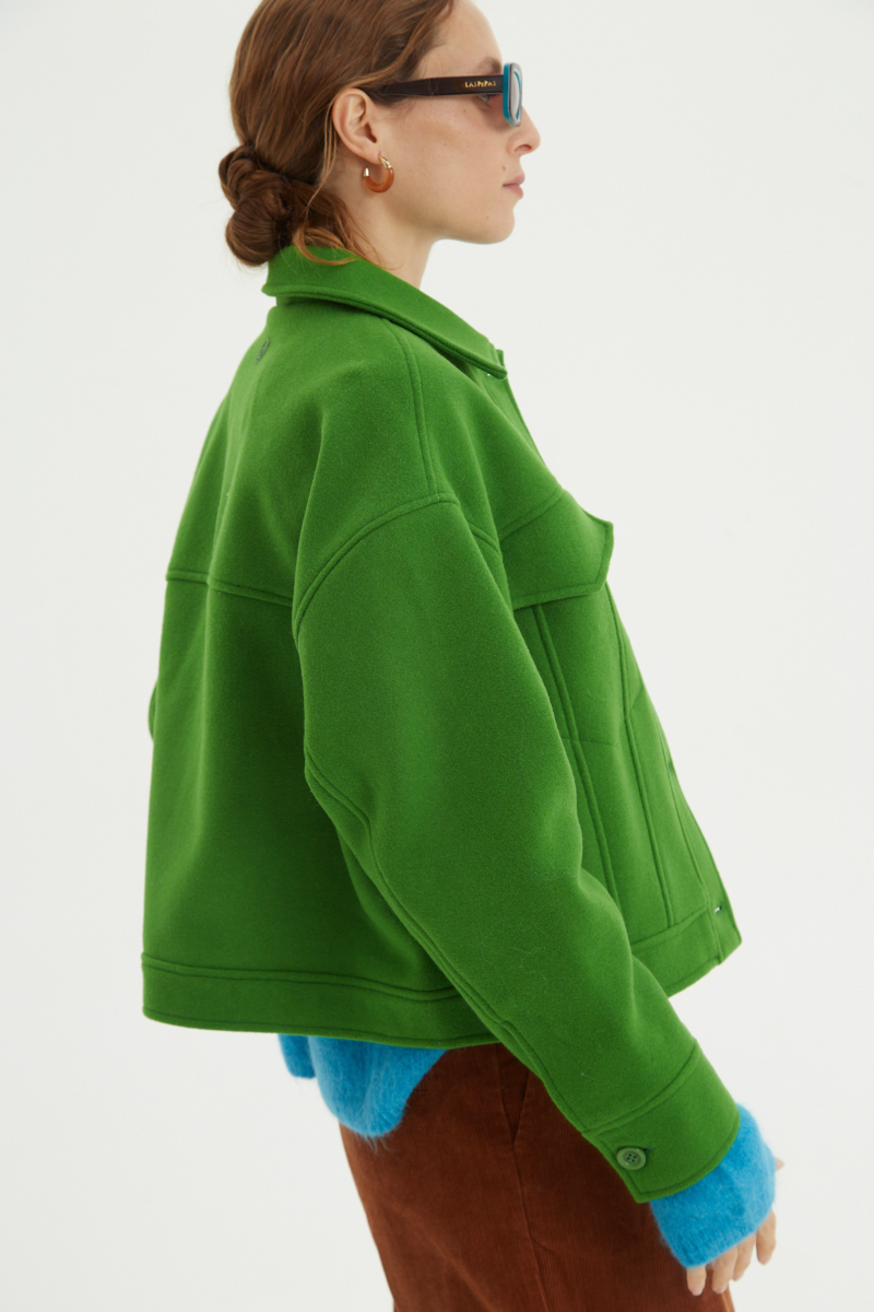 Campera verde de lana recta y larga hasta la cadera con sisas caídas, cuello en punta, botones a tono y bolsillos delanteros con solapa. 