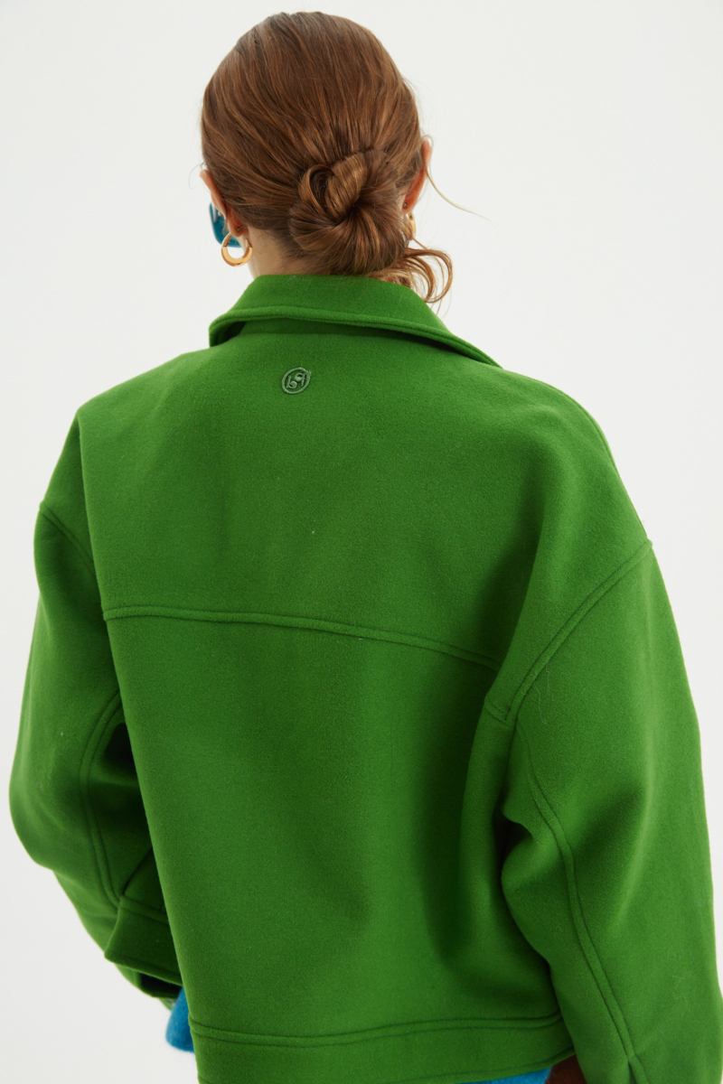 Campera verde de lana recta y larga hasta la cadera con sisas caídas, cuello en punta, botones a tono y bolsillos delanteros con solapa. 