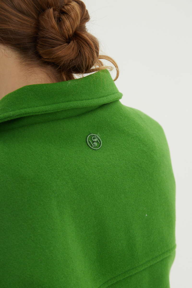 Campera verde de lana recta y larga hasta la cadera con sisas caídas, cuello en punta, botones a tono y bolsillos delanteros con solapa. 
