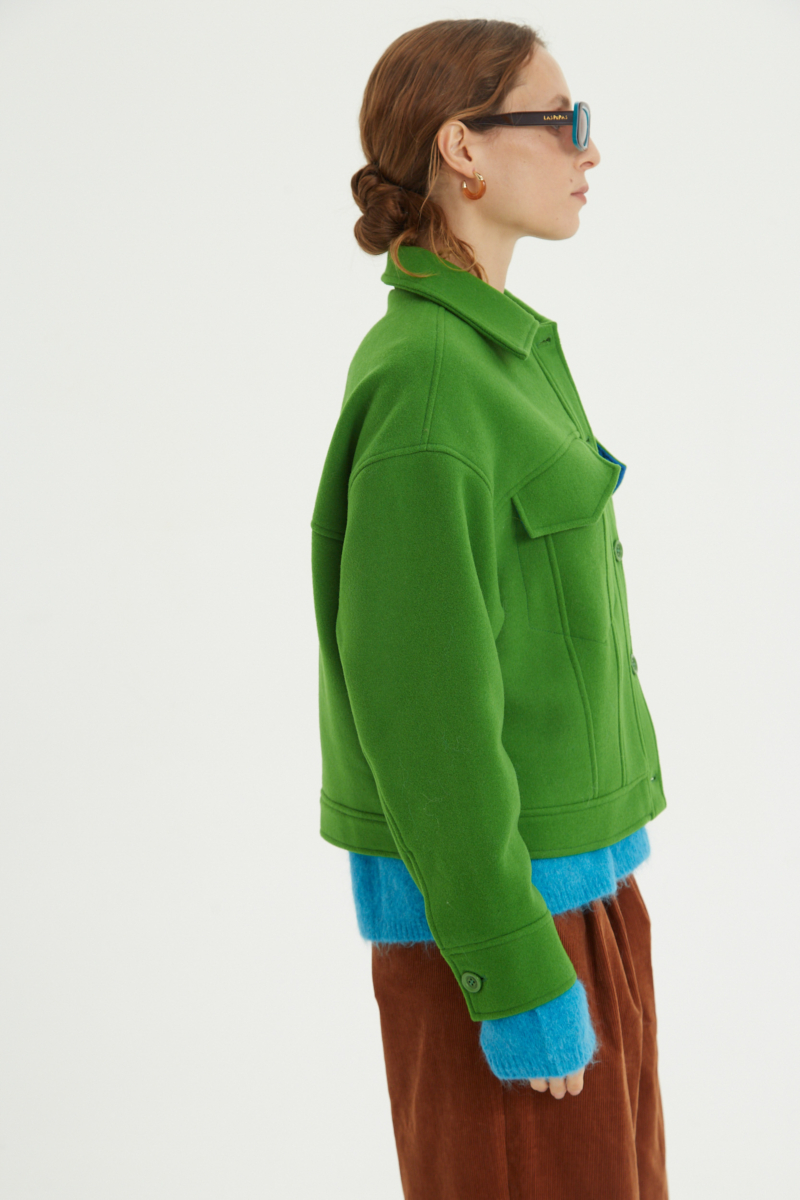 Campera verde de lana recta y larga hasta la cadera con sisas caídas, cuello en punta, botones a tono y bolsillos delanteros con solapa. 
