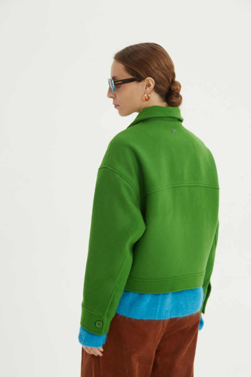Campera verde de lana recta y larga hasta la cadera con sisas caídas, cuello en punta, botones a tono y bolsillos delanteros con solapa. 