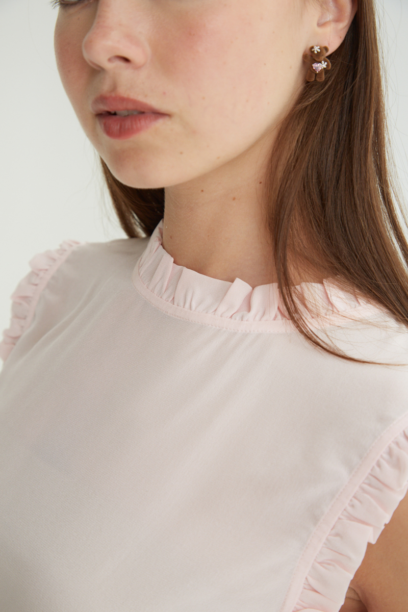 Musculosa rosa de seda con volados en cuello y sisas, de corte recto y larga a la cadera con cuello mao y botones en la espalda. 
