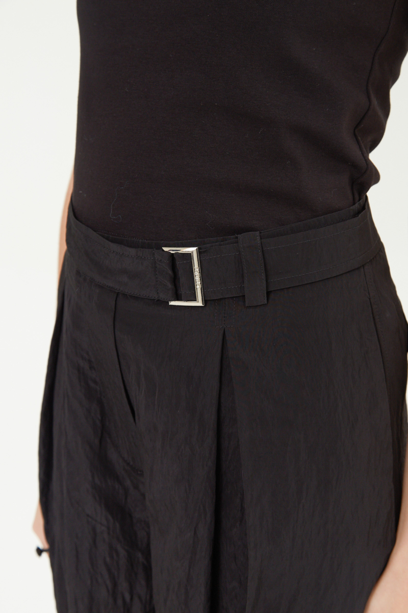 Pantalón negro con textura arrugada y brillo sutil, con pinza en la pierna ajustada al tobillo, cintura con cinturón y bolsillos traseros.