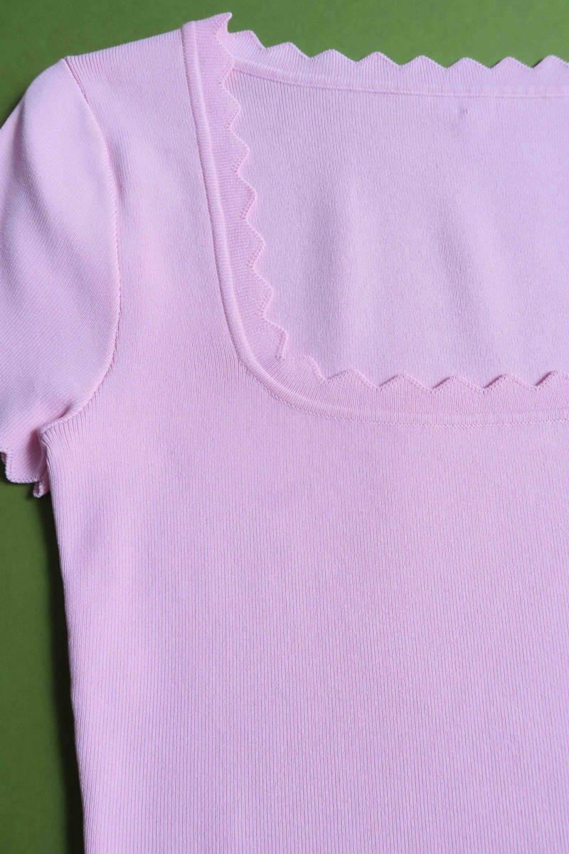 Remera rosa tejida  con terminación ondulada en mangas, ruedo y escote, de escote cuadrado y corte recto larga a la cadera. 