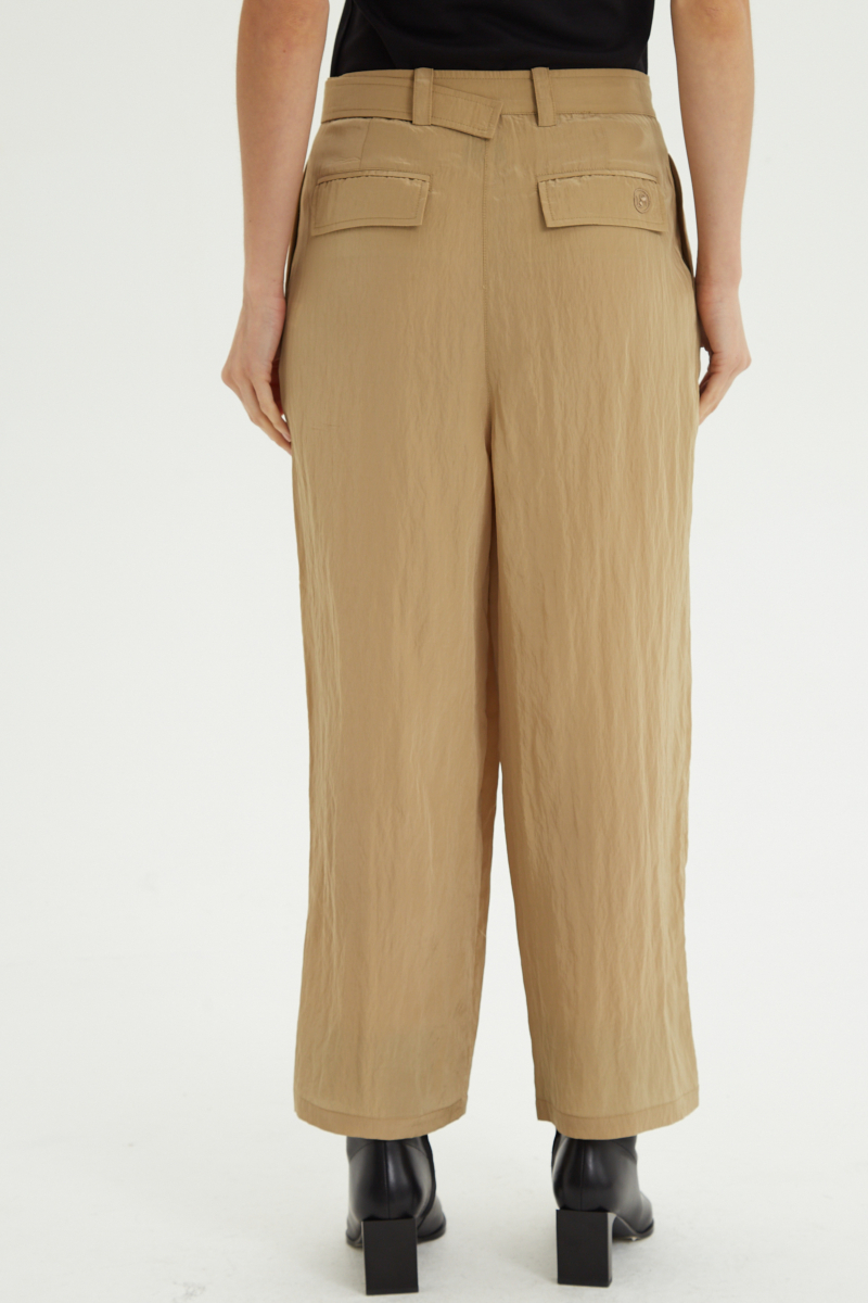 Pantalón beige con textura arrugada y brillo sutil, con pinza en la pierna ajustada al tobillo, cintura con cinturón y bolsillos traseros.