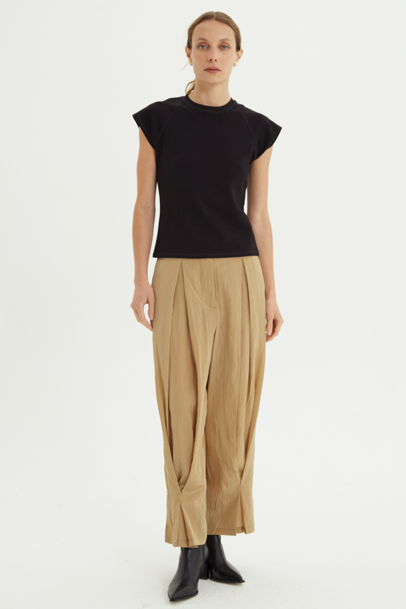 Pantalón beige con textura arrugada y brillo sutil, con pinza en la pierna ajustada al tobillo, cintura con cinturón y bolsillos traseros.