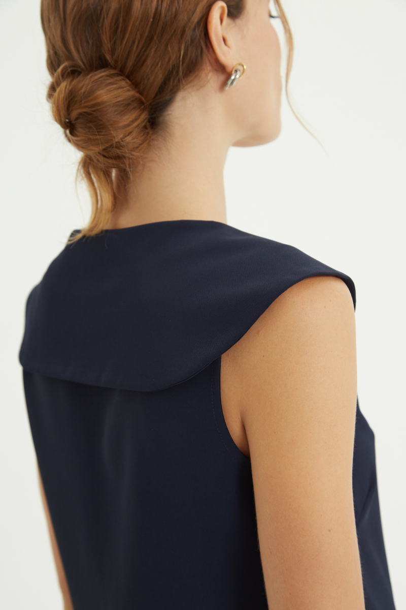 Top azul sastrero con cuello marinero y escote en V, de corte recto largo a la cadera con pinzas frontales y botones a tono.