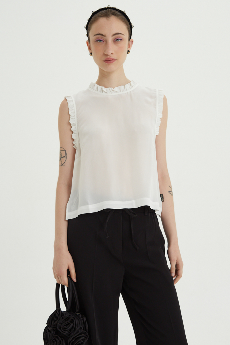 Musculosa cruda de seda con volados en cuello y sisas, de corte recto y larga a la cadera con cuello mao y botones en la espalda. 
