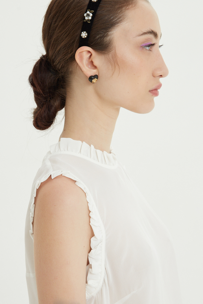 Musculosa cruda de seda con volados en cuello y sisas, de corte recto y larga a la cadera con cuello mao y botones en la espalda. 
