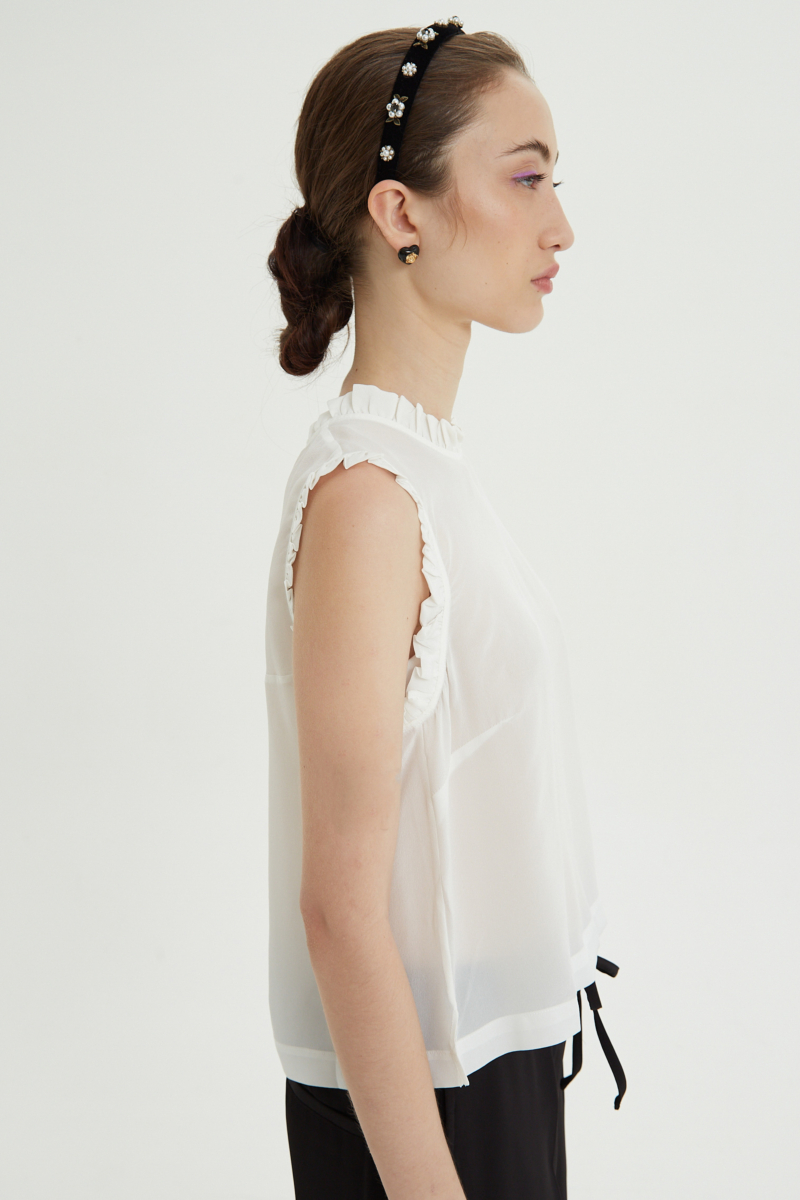 Musculosa cruda de seda con volados en cuello y sisas, de corte recto y larga a la cadera con cuello mao y botones en la espalda. 
